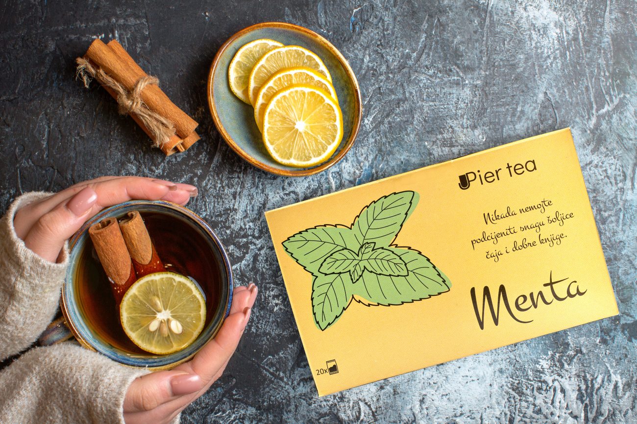 Above view of fresh lemons and hand holding a cup of black tea with cinnamon on dark background